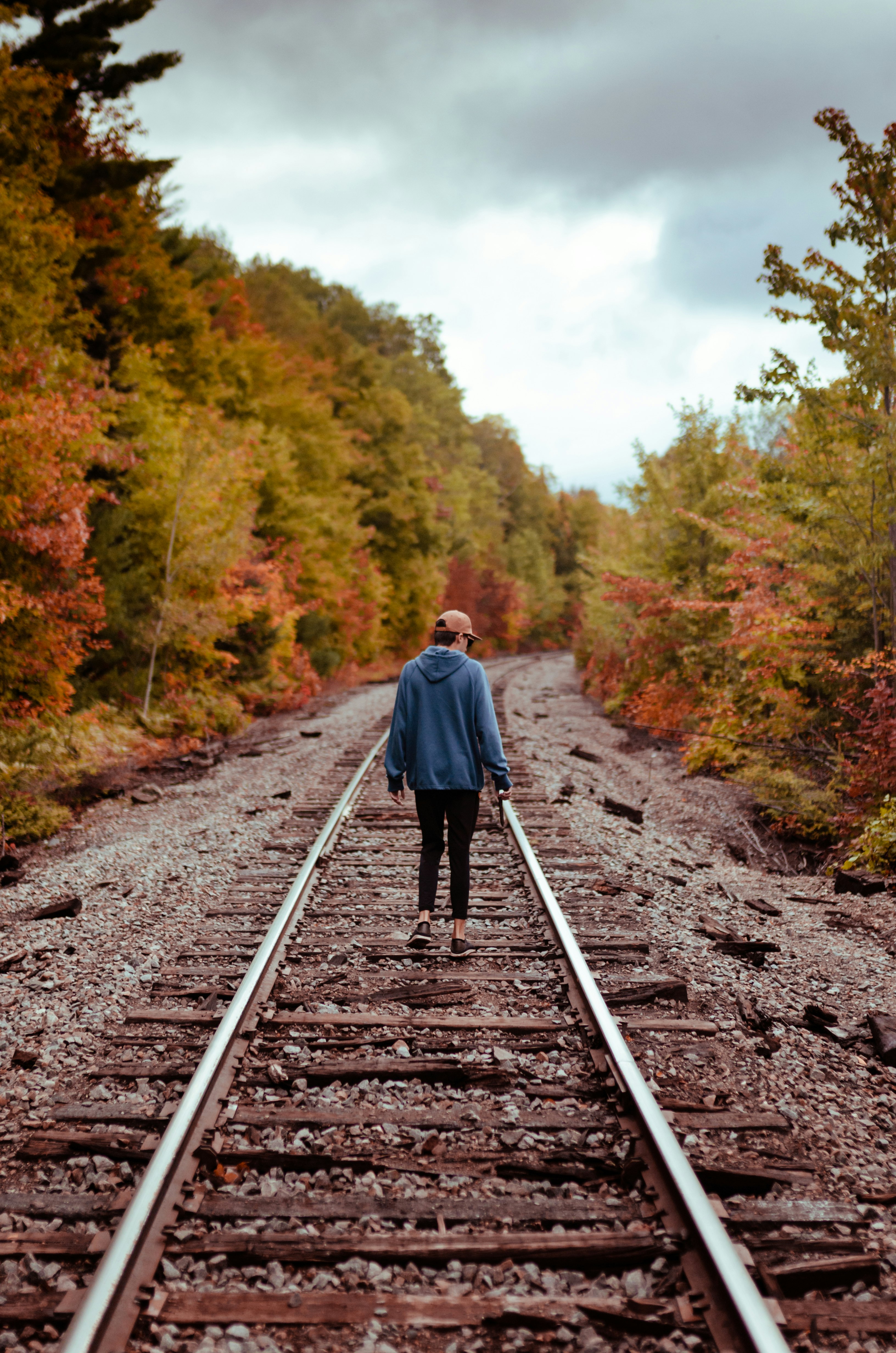 woman in blue hoodie walking on train rail during daytime